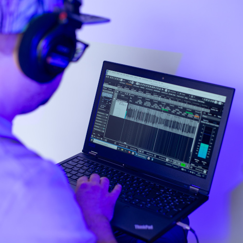 Abbildung Konstantin Schulz von hinten mit Kopfhörern auf Laptop schauend, wo ein Bearbeitungsprogramm offen ist