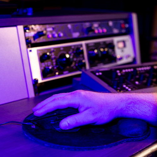 Abbildung rechte Hand auf Maus, im Hintergrund Geräte zur Audiobearbeitung